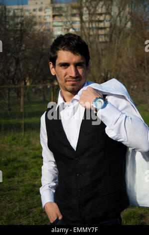 Jung, gut aussehend und Mode Mann mit glattem Haar außerhalb trägt eine schwarze Weste, weißes Hemd, Armbanduhr, schaut in die Kamera Stockfoto