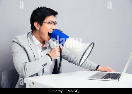 Geschäftsmann am Tisch sitzen und schreiend in Megaphon auf laptop Stockfoto