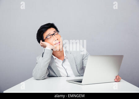 Junge asiatische Geschäftsmann Sleepig am Tisch mit Laptop über grauen Hintergrund Stockfoto