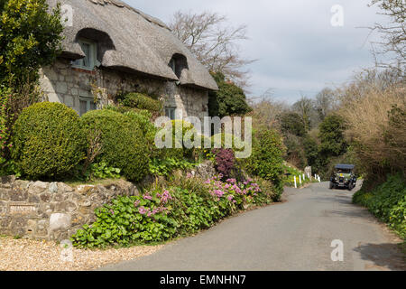 Ein grüner Oldtimer nähert sich eine schmale Gasse in Richtung eine strohgedeckte Hütte in Godshill, Isle Of Wight Stockfoto