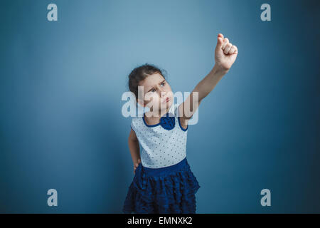 eine Mädchen von sieben europäischen Aussehen Brünette hält Finger Objekt auf einem grauen Hintergrund Stockfoto