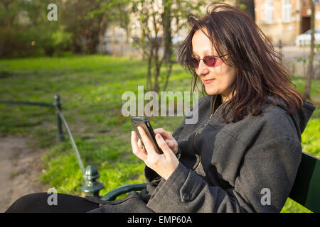 Junge Frau sitzt auf einer Parkbank spricht per Telefon. Stockfoto