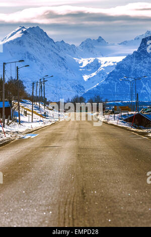 Eine sonnige norwegische Landschaft mit einer Landstraße im Vordergrund und Snowy und blau Gebirge im Hintergrund. Stockfoto