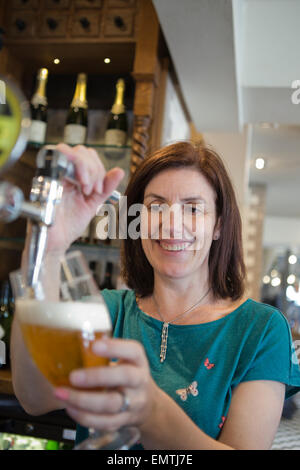 Eine Frau hinter einer Bar ziehen einen Pint Lager während lächelnd Stockfoto