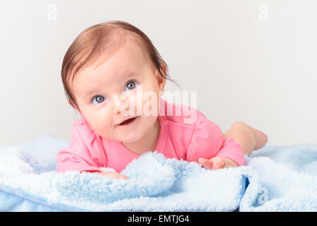 Kleines lächelndes Mädchen am Bauch, auf blaue Decke liegen. Sie trägt rosa Anzug Körper und Blick in die Kamera Stockfoto