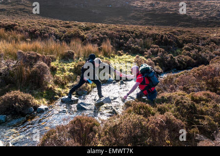 Wanderer durchqueren ein Gebirgsbach auf Slievetooey Voralpen nahe Ardara, County Donegal, Irland Stockfoto
