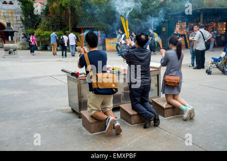 drei Personen Räucherstäbchen beten auf den Knien, am Po Lin Monastery, in Hongkong, China Stockfoto