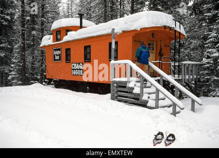 Schneeschuhwandern Gast betritt seine Wohnung, die einem restaurierten 1895 Eisenbahn Dienstwagen, einer der acht historische Caboose Triebwagen, die Hauptattraktionen im Izaaka Walton Inn am Rande des Glacier National Park in Montana, USA. Das Orange lackierte Auto von der Chicago, Burlington und Quincy Linie verfügt nun über eine Full-Size-Bett, Bad mit Dusche und gut ausgestattete Küchenzeile. Das remote Inn ist ganzjährig geöffnet und auf der Schiene mit Amtrak, Amerikas große Passagierservice Schiene erreicht. Stockfoto