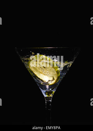 Martini-Glas und alkoholisches Getränk mit einer Limettenscheibe, Spritzer, schwarzer Hintergrund Stockfoto