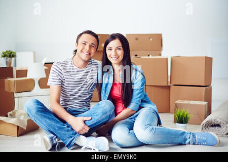 Glückliches junges Paar sitzt auf dem Boden der neuen Wohnung im Hintergrund der Boxen Stockfoto