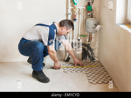 Mann mittleren Alters-Arbeiter in blauer Hose und grau legt T-shirt auf den Fliesen im Raum des neuen Hauses Stockfoto