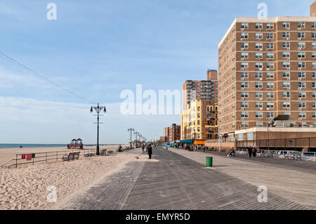 Die Menschen sitzen auf Bänken in der Sonne und gehen vor einem Mehrfamilienhaus auf der Promenade in Brighton Beach, Brooklyn NY Stockfoto