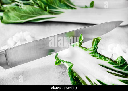 Eine Nahaufnahme von einem Messer hacken frische Bok Choi auf Marmor Hintergrund. Stockfoto