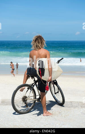 Brasilianische Surfer auf einem Fahrrad sitzen auf Fahrrad mit Blick auf die Wellen Ipanema Strand Rio de Janeiro Brasilien Stockfoto