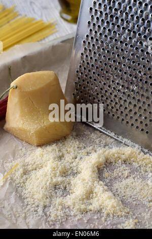 Close-up geriebener Parmesan-Käse und Metall-Reibe auf Holztisch. Stockfoto