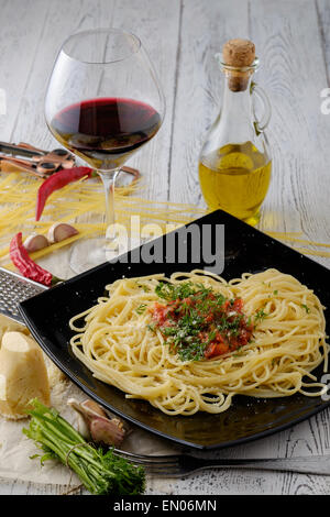 Italienischer Pasta gekocht im rustikalen Stil mit einer Sauce aus frischen Tomaten und Knoblauch auf einem Holztisch mit einem Glas Rotwein. Stockfoto