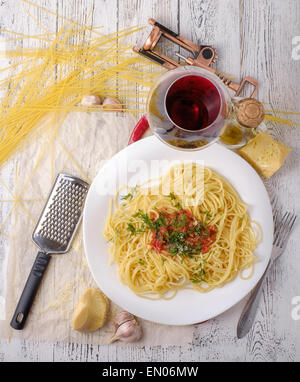 Italienischer Pasta gekocht im rustikalen Stil mit einer Sauce aus frischen Tomaten und Knoblauch auf einem Holztisch mit einem Glas Rotwein. Stockfoto