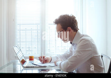 junger Geschäftsmann, die Arbeit mit Dokumenten und Laptop in hellen Büroeinrichtung Stockfoto