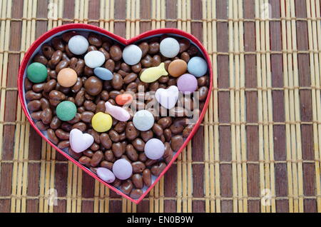 Herz geformten Box gefüllt mit kleinen Pralinen Kugeln auf dem Tisch aus Holz Bambus Stockfoto