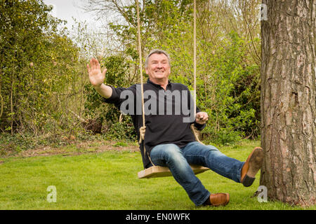 Senior woman winken während auf einer Baum-Schaukel im Garten Stockfoto