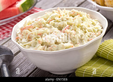 Eine Schüssel mit leckeren cremigen hausgemachten Krautsalat auf einem rustikalen Picknick-Tisch mit Wassermelone und Mais. Stockfoto