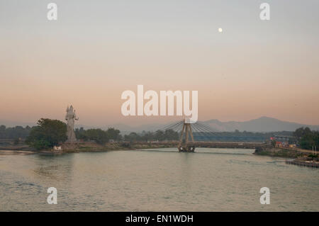 Indien, Uttaranchal, Haridwar, Sonnenuntergang über den Ganges-Fluss mit Brücke und Shiva-statue Stockfoto