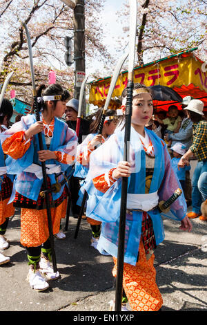 Ein Team von Kindern, Mädchen, die als Shimobe-Soldaten der Heian-Ära verkleidet in der Frühlingsparade unter Kirschblüten in Tada, Japan marschieren. Stockfoto