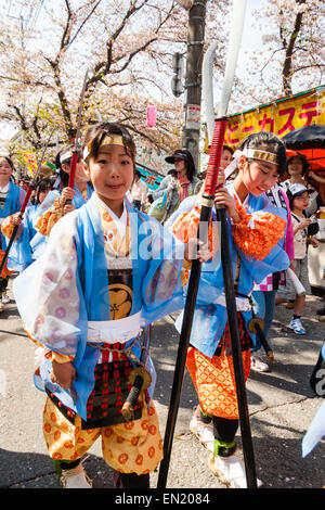 Ein Team von Kindern, Mädchen, die als Shimobe-Soldaten der Heian-Ära verkleidet in der Frühlingsparade unter Kirschblüten in Tada, Japan marschieren. Stockfoto