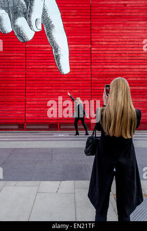 Eine Frau posiert für Fotos unter einem riesigen Cartoon Finger außerhalb der National Gallery, South Bank, London, England Stockfoto