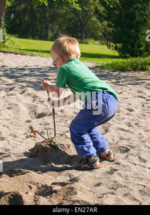 Drei Jahre alter Junge auf Spielplatz, Veredelung eine Sandburg indem man Stöcke für Dekoration, Oslo Norwegen Stockfoto