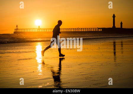 Männliche Jogger Whitby mit am Strand die Sonne über die Piers in Bachground. Whitby, North Yorkshire, UK Stockfoto