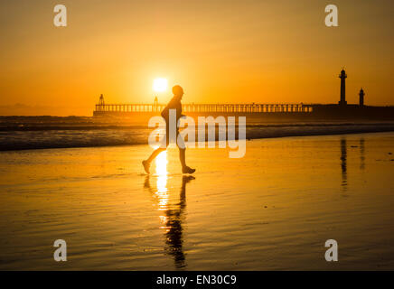 Männliche Jogger Whitby mit am Strand die Sonne über die Piers in Bachground. Whitby, North Yorkshire, UK Stockfoto