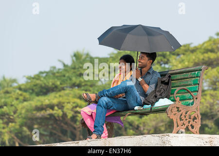 Junges Paar mit einem Sonnenschirm sitzen auf einer Parkbank, Fort Kochi, Kerala, Indien Stockfoto