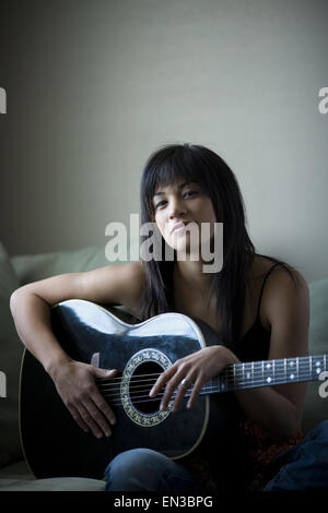 Frau sitzt auf dem Sofa hält lächelnd Gitarre Stockfoto