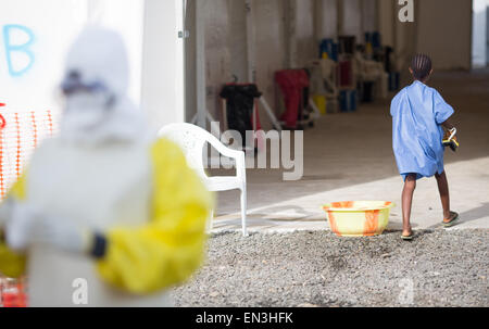 Monrovia, Liberia. 9. April 2015. Ein Mädchen für Malaria behandelt geht außerhalb einer Krankenstation SITTU (schwere Infektionen vorübergehend Behandlungseinheit) in der Nähe eines Bediensteten tragen von Schutzkleidung in Monrovia, Liberia, 9. April 2015. Foto: Kay Nietfeld/Dpa/Alamy Live News Stockfoto