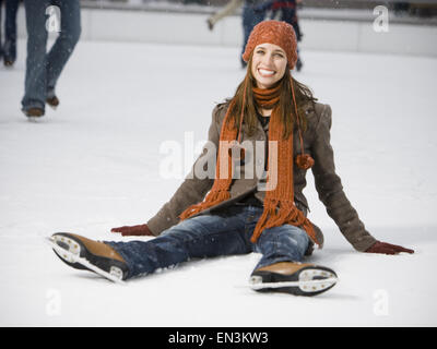 Frau mit Skates sitzen auf Eis lächelnd Stockfoto