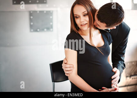 Mann seine schwangere Frau zu küssen am Hals. Schöne und elegante Mann und Frau. Junge Familie. Stockfoto