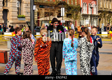 Clown mit bemaltem Gesicht, rote Nase und trägt einen Hut unterhalten Kinder gekleidet in Onesies in der Guildhall Square, Derry, Lon Stockfoto