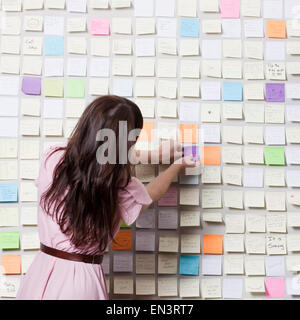 Studioaufnahme jungen Frau Wand bedeckt in Klebstoff Notizen Notizen aufsetzen Stockfoto