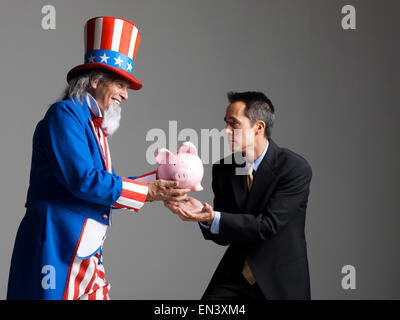 Mann in Uncle Sam Kostüm geben Sparschwein zu anderen Menschen, Studio gedreht Stockfoto