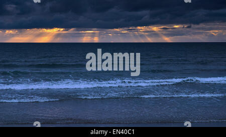 Sonnenuntergang am Strand in Ynyslas, Wales als die Sonne glänzt Sonnenstrahlen auf das Meer unter schweren dunklen Wolken. Stockfoto