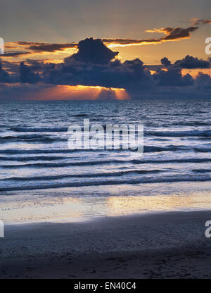 Sonnenuntergang am Strand in Ynyslas, Wales als die Sonne glänzt Sonnenstrahlen auf das Meer unter schweren dunklen Wolken. Stockfoto