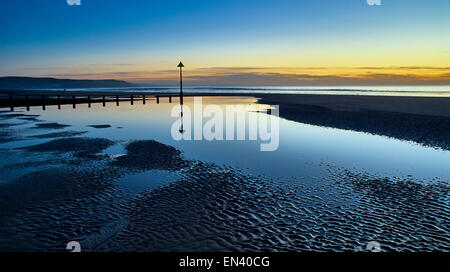 Reflexionen der Buhnen am Strand in Ynyslas, Wales bei Sonnenuntergang in den Felsen-Pool erstellt von der zurückweichenden Flut gezeigt. Stockfoto