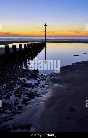 Reflexionen der Buhnen am Strand in Ynyslas, Wales bei Sonnenuntergang in den Felsen-Pool erstellt von der zurückweichenden Flut gezeigt. Stockfoto