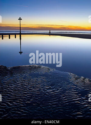 Eine Person, die einen Hund am Strand in Ynyslas, Wales bei Sonnenuntergang im Rock Pool durch die abziehenden Flut spiegelt. Stockfoto