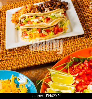 Ein Teller mit Tacos mit Salat, Tomaten, Avocado und Koriander auf einem Bambus-Ladegerät Stockfoto