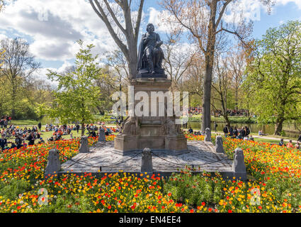 Vondelpark Amsterdam. Die Statue der Dramatiker Joost van Den Vondel mit orange Tulpen und Menschen im Vondel Park im Frühjahr Stockfoto