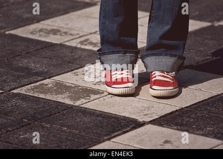 Beine des jungen Teenager weiblich in Red Sneakers stehen auf der Straße im Schach wie karierte Pflaster, getönten Bild mit Selective Stockfoto