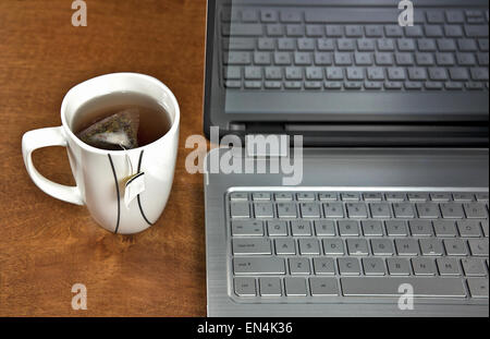 Teebeutel in heißes Wasser mit Laptop auf Holztisch. Stockfoto