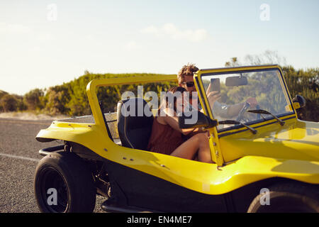 Junge glückliche Paar Roadtrip in ihrem Auto mit Frau, die ein Selbstporträt von ihrem Handy genießen. Stockfoto